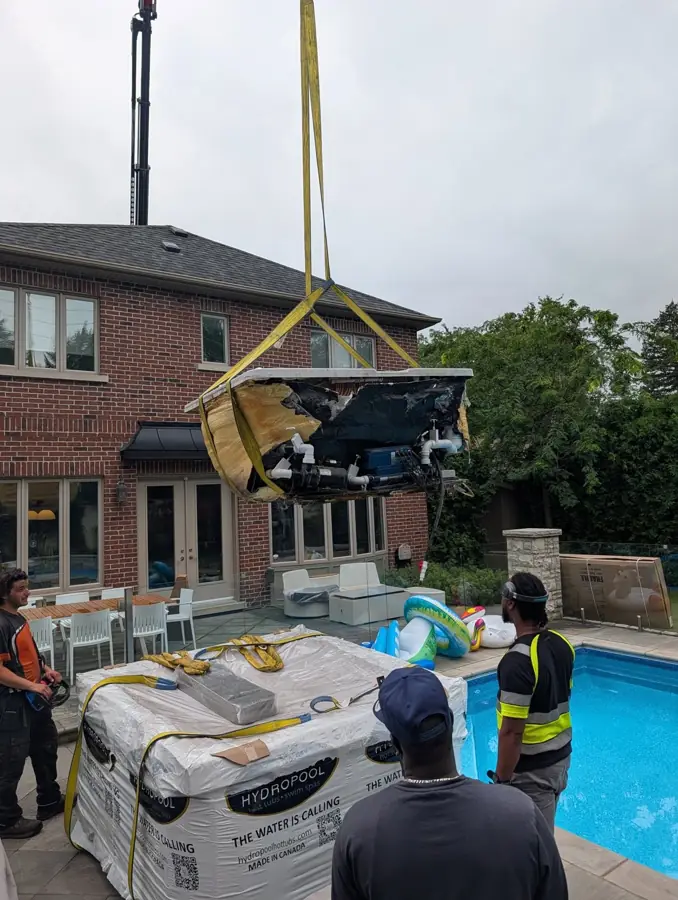 Crane lifting a hot tub over a house into a Toronto backyard